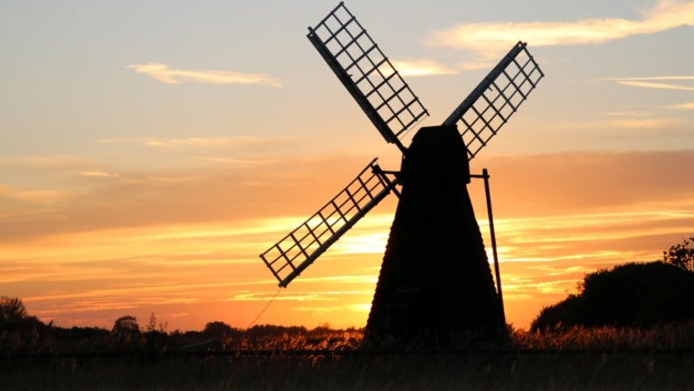 An orange evening sky with a windmill silhouetted in the foreground